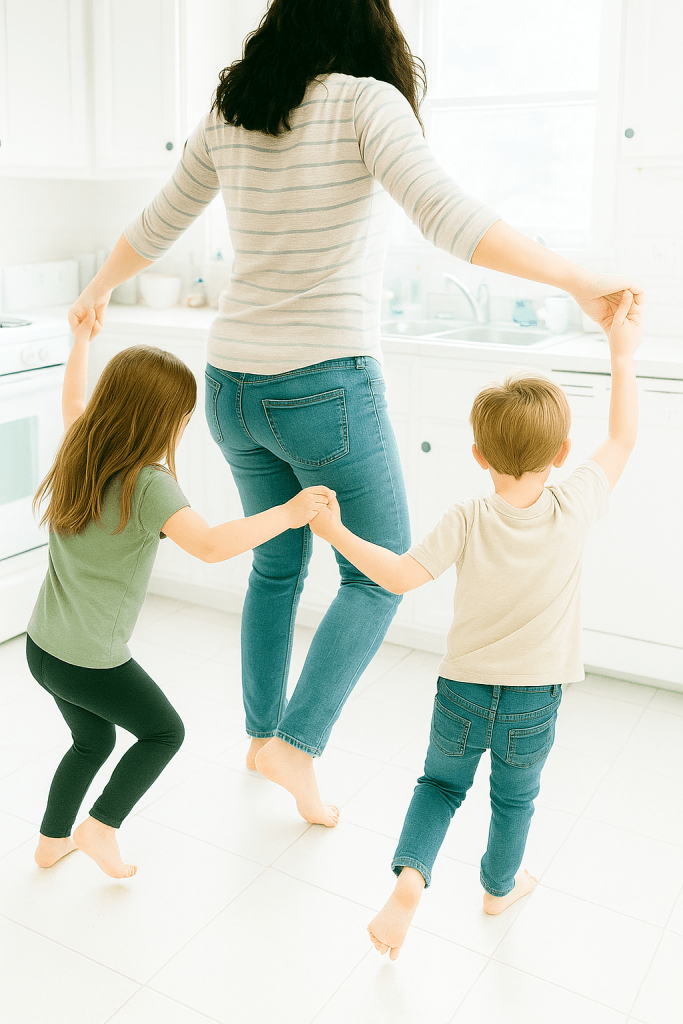 A woman and two children dancing together in a bright kitchen, all barefoot and holding hands, conveying a joyful and playful atmosphere.